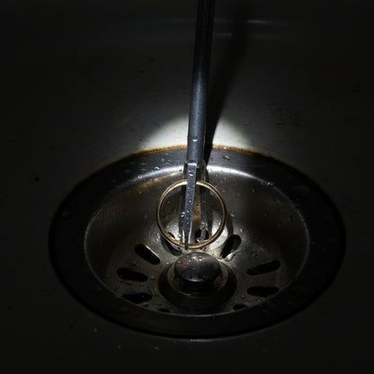 Four steel claws of the drain grabber tool inserted into a bathroom shower drain
