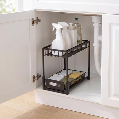 A black metal two-tier pull-out organizer basket inside a white kitchen cabinet, holding cleaning spray bottles and sponges.