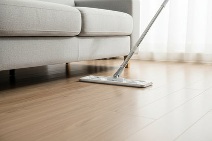 Flat mop head sliding under a grey sofa on hardwood floor showing low profile swivel head