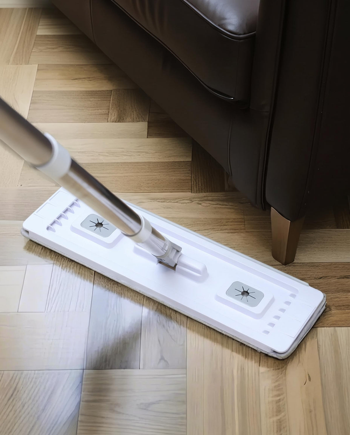 Flat mop head lying flat on a hardwood floor, swivelling to reach under a dark sofa