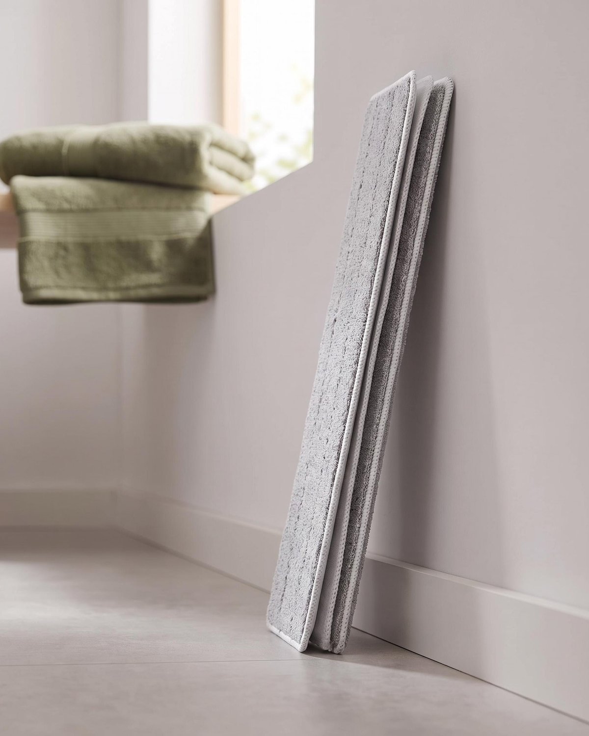 Three thick grey three-layer microfiber mop pads leaning against a wall in a laundry room